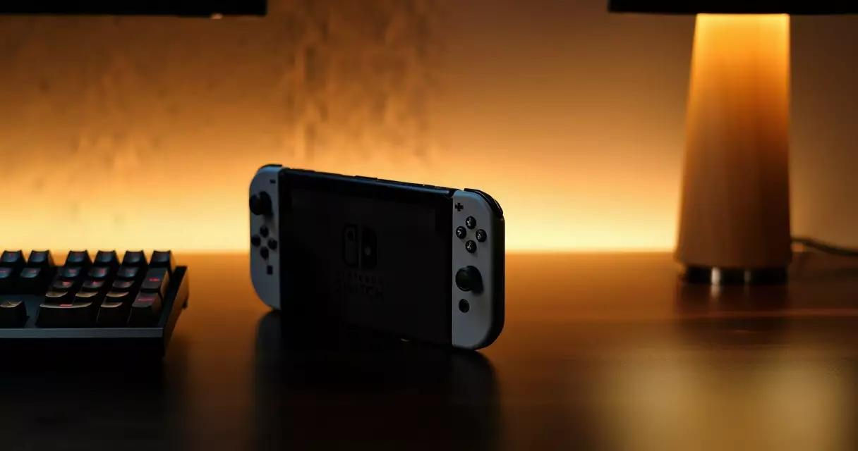 Nintendo Switch console beside mechanical keyboard on dark gaming desk with warm ambient side lighting