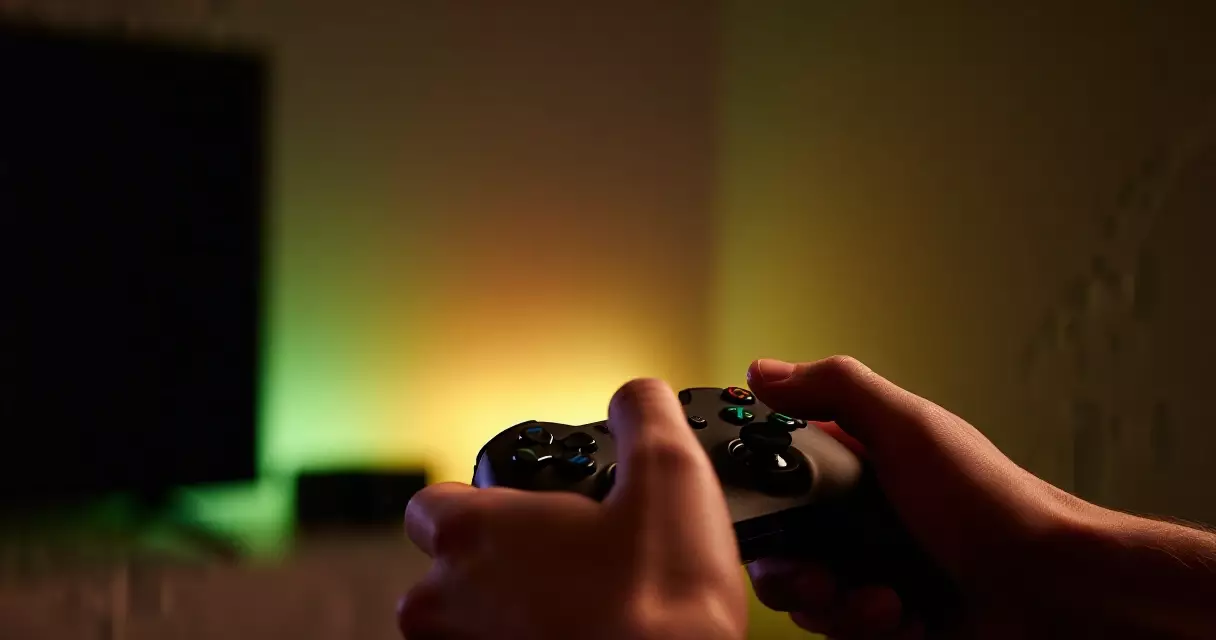 Player holding a gaming controller in ambient lit room enjoying a live-service game