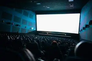 A crowded cinema audience seated in a theater watching a movie on a large screen.