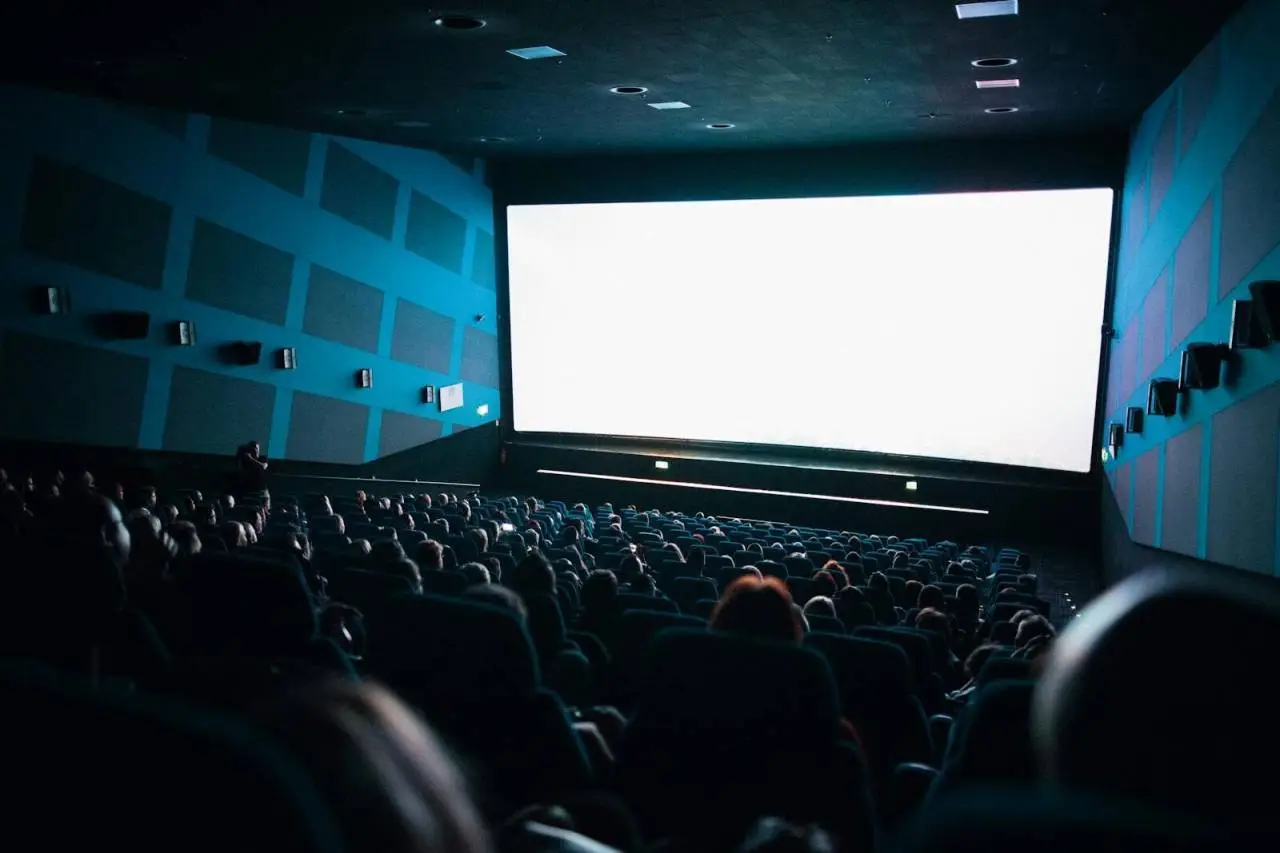 A crowded cinema audience seated in a theater watching a movie on a large screen.