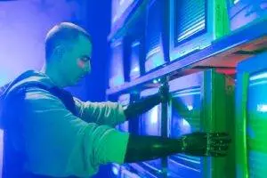 Man with prosthetic arms interacting with stack of CRT televisions, showcasing technology.